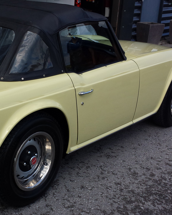 Hellgelbes Oldtimer-Cabrio mit schwarzem Verdeck von der Seite gezeigt