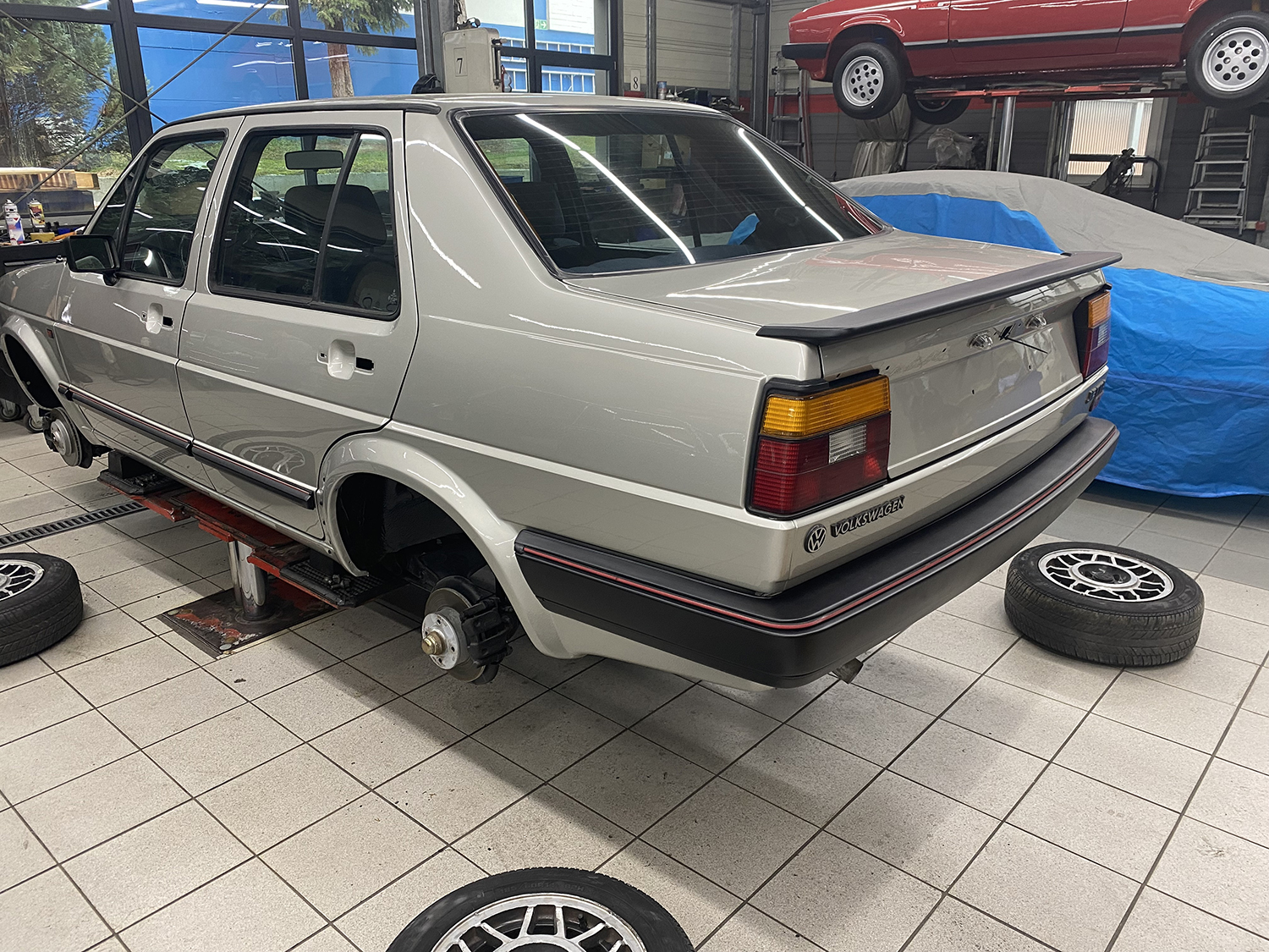 Silberner VW-Oldtimer in einer Werkstatt auf Hebebühne, ohne Räder und teils demontiert