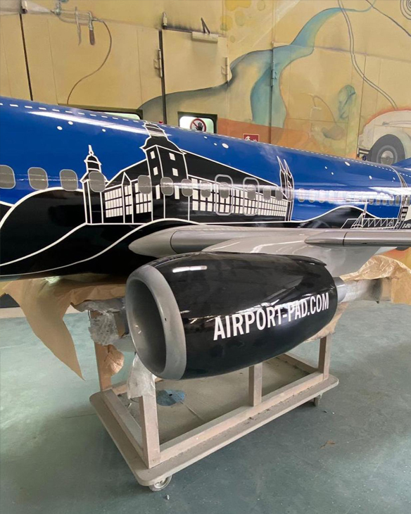 Bemaltes Flugzeugrumpfmodell mit Triebwerk, auf einem Gestell in einer Werkstatt