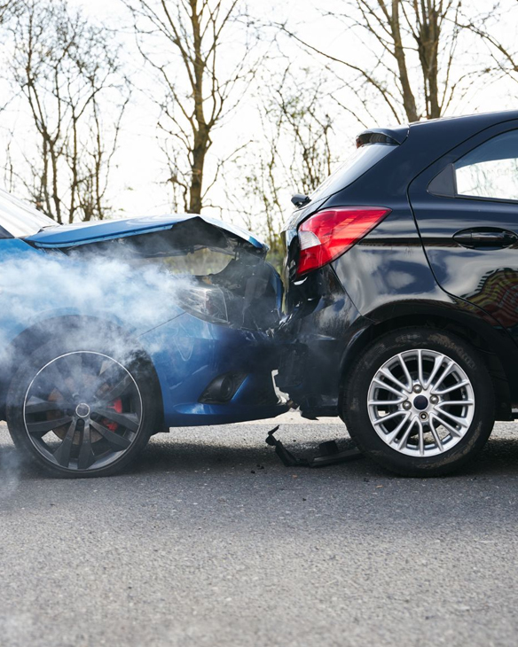 Zwei Autos nach einem Heckaufprall, die blaue Front ist stark beschädigt und es steigt Rauch auf