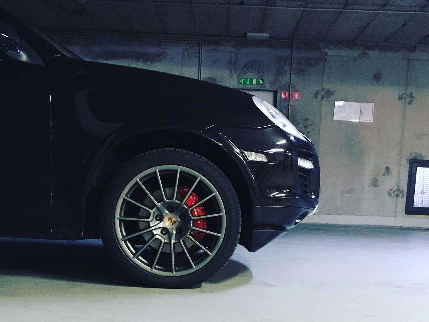 Schwarzes Porsche-SUV in einer Tiefgarage, mit Frontrad und rotem Bremssattel im Fokus