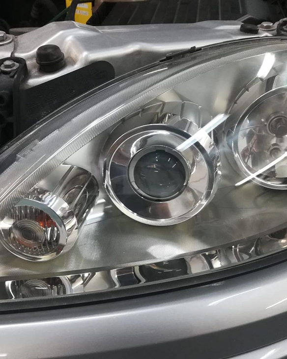 Nahaufnahme eines silbernen Auto-Scheinwerfers mit runden Chrom-Reflektoren und klarer Abdeckung