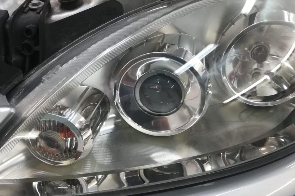 Nahaufnahme eines glänzenden Autoscheinwerfers mit mehreren runden Linsen und Reflektoren