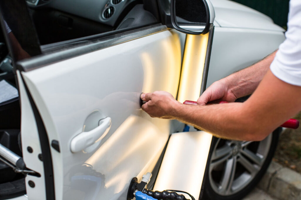 Mann entfernt mit einem Saugnapf eine Delle an der weißen Autotür