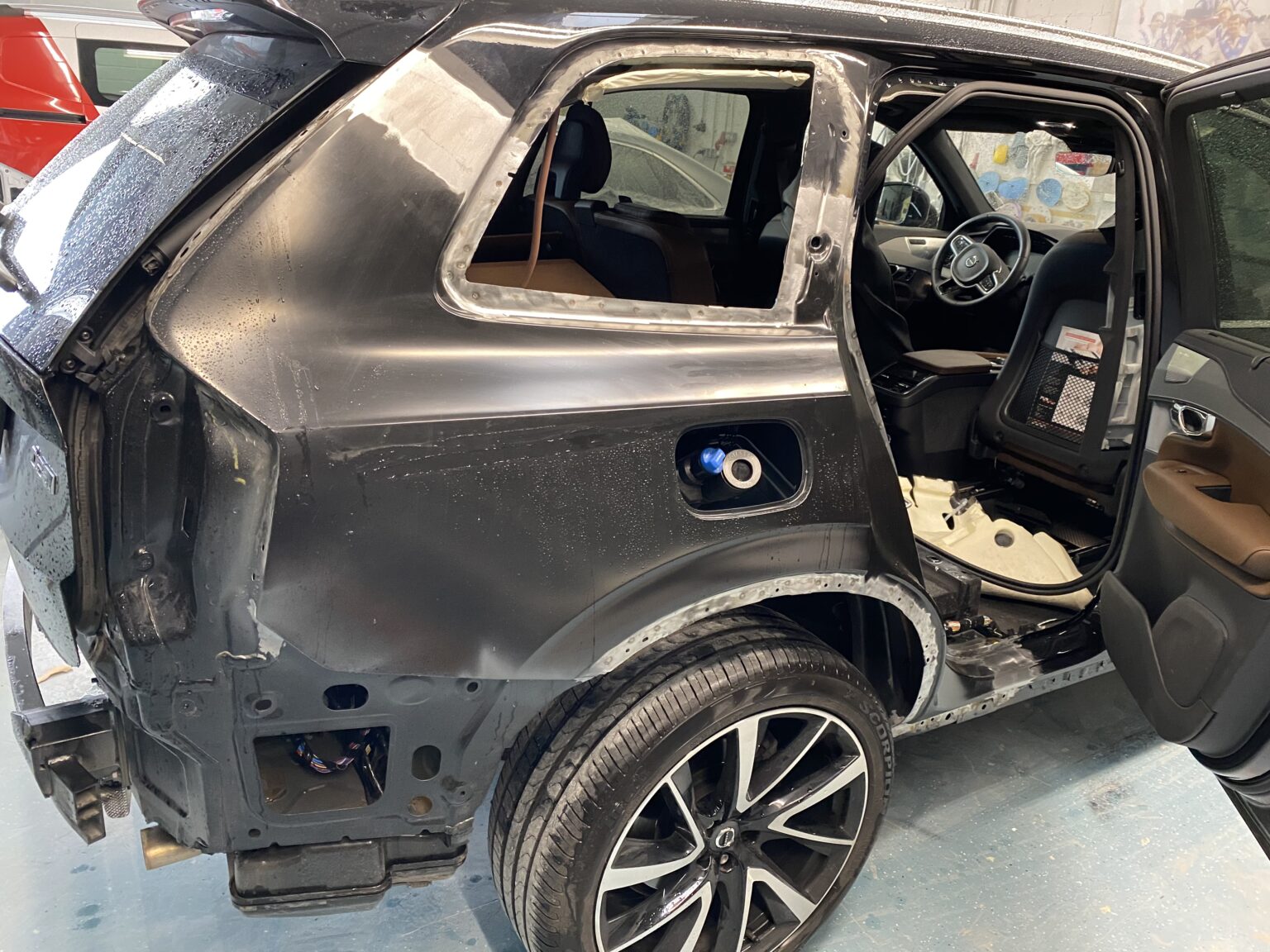 Schwarzer SUV in der Werkstatt mit demontierter Seitenkarosserie und offener Tür, innen teilweise freigelegt