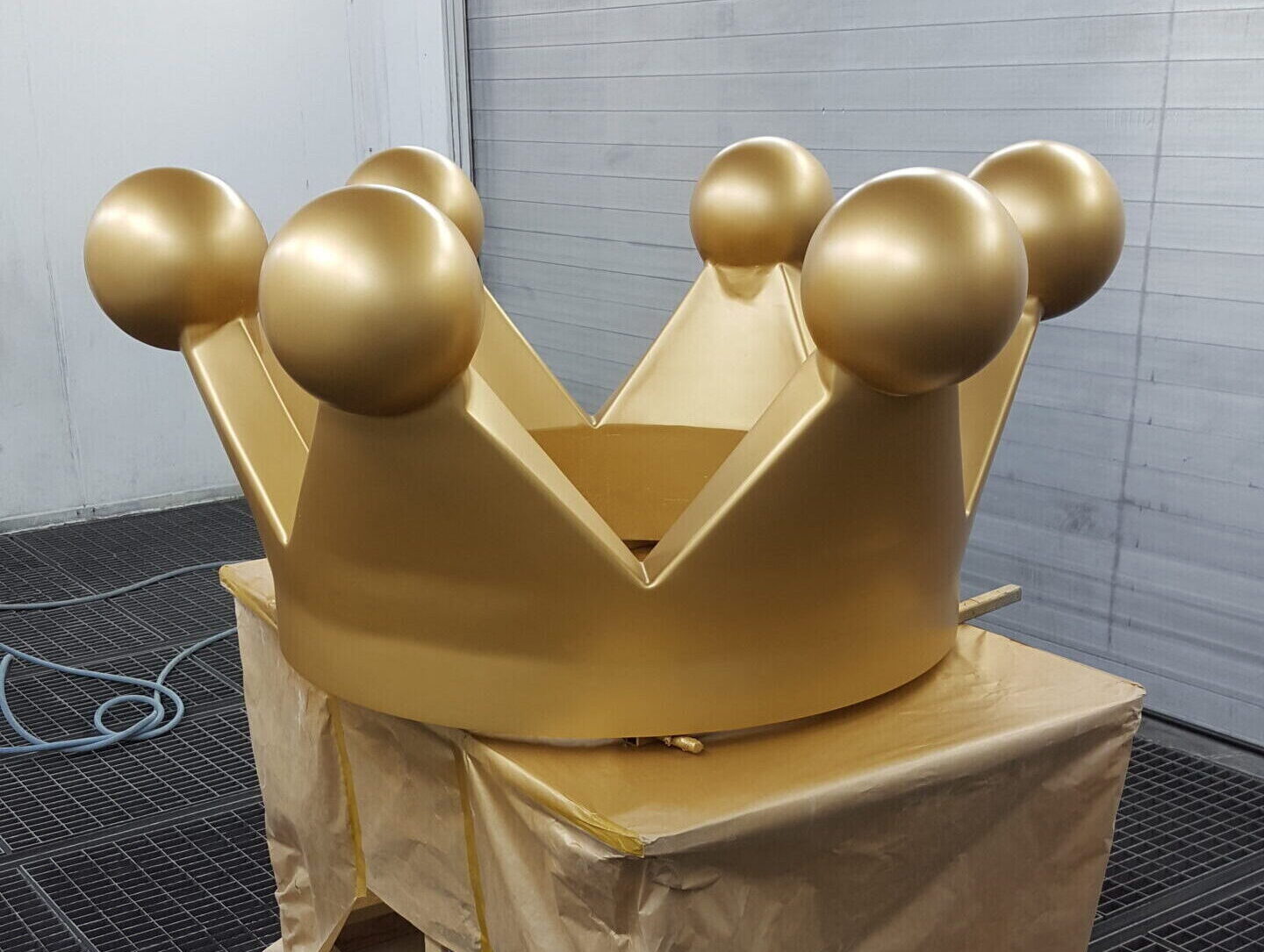 Goldfarbene Kronenskulptur in einer Werkstatt, auf einem abgedeckten Unterbau steht
