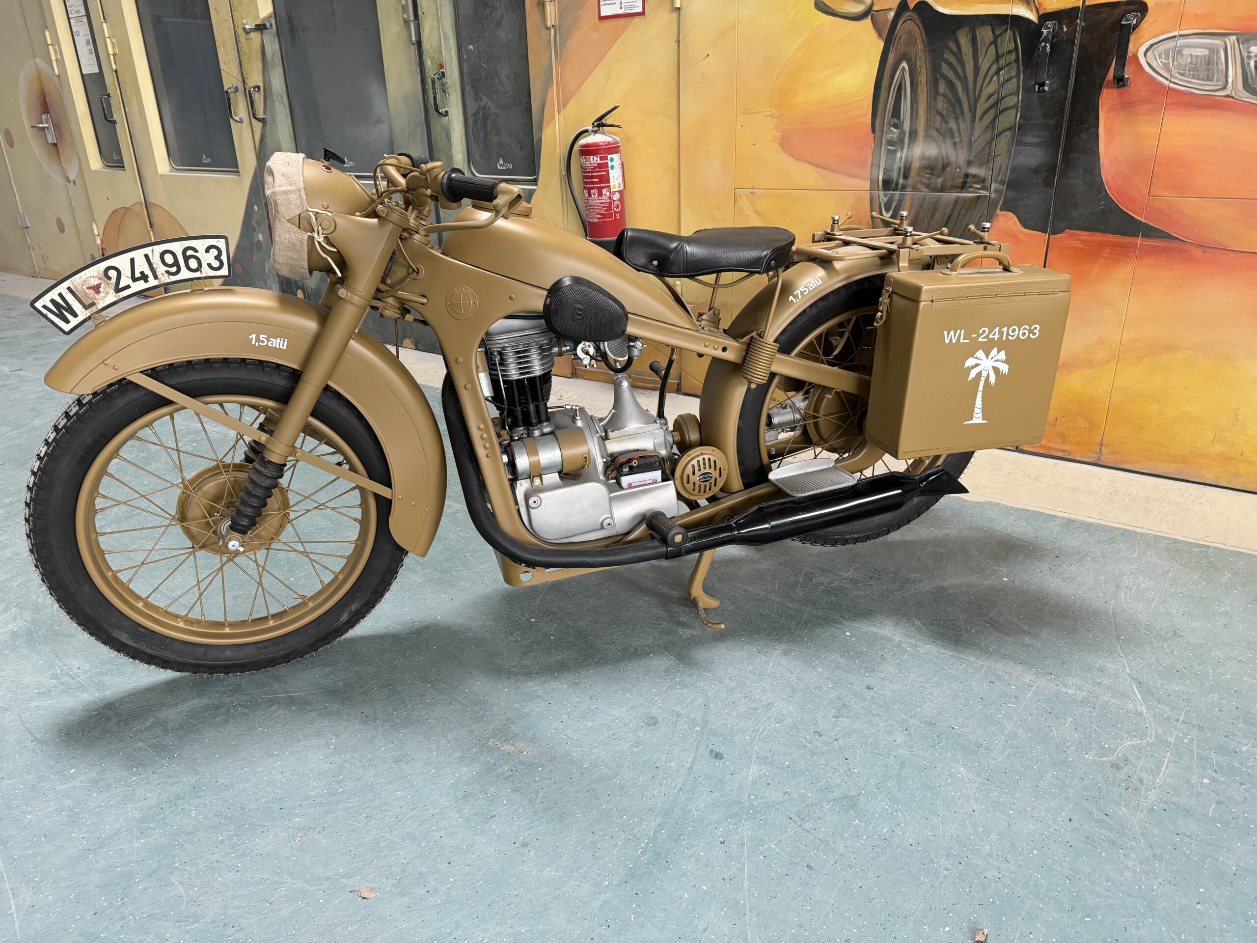 Sandfarbenes BMW-Motorrad mit Seitenkoffer und Militärkennzeichen in einer Ausstellungshalle