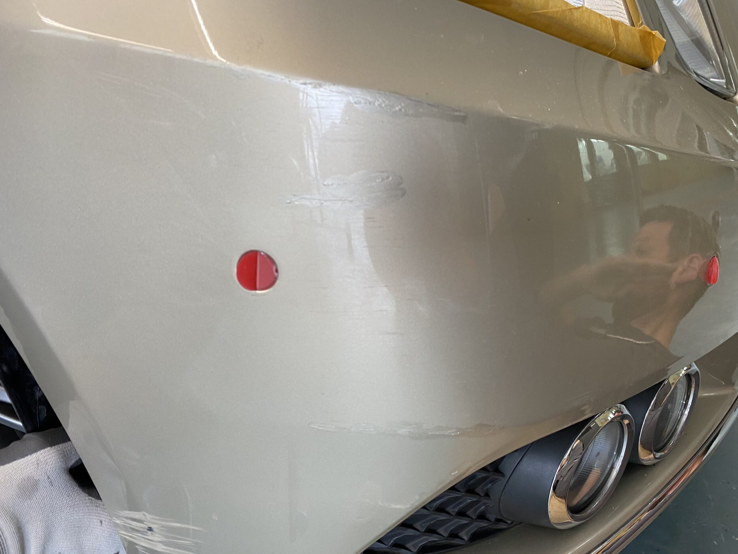 Nahaufnahme einer lackierten Autostoßstange mit Kratzern, Abdeckband und zwei roten Markierungspunkten