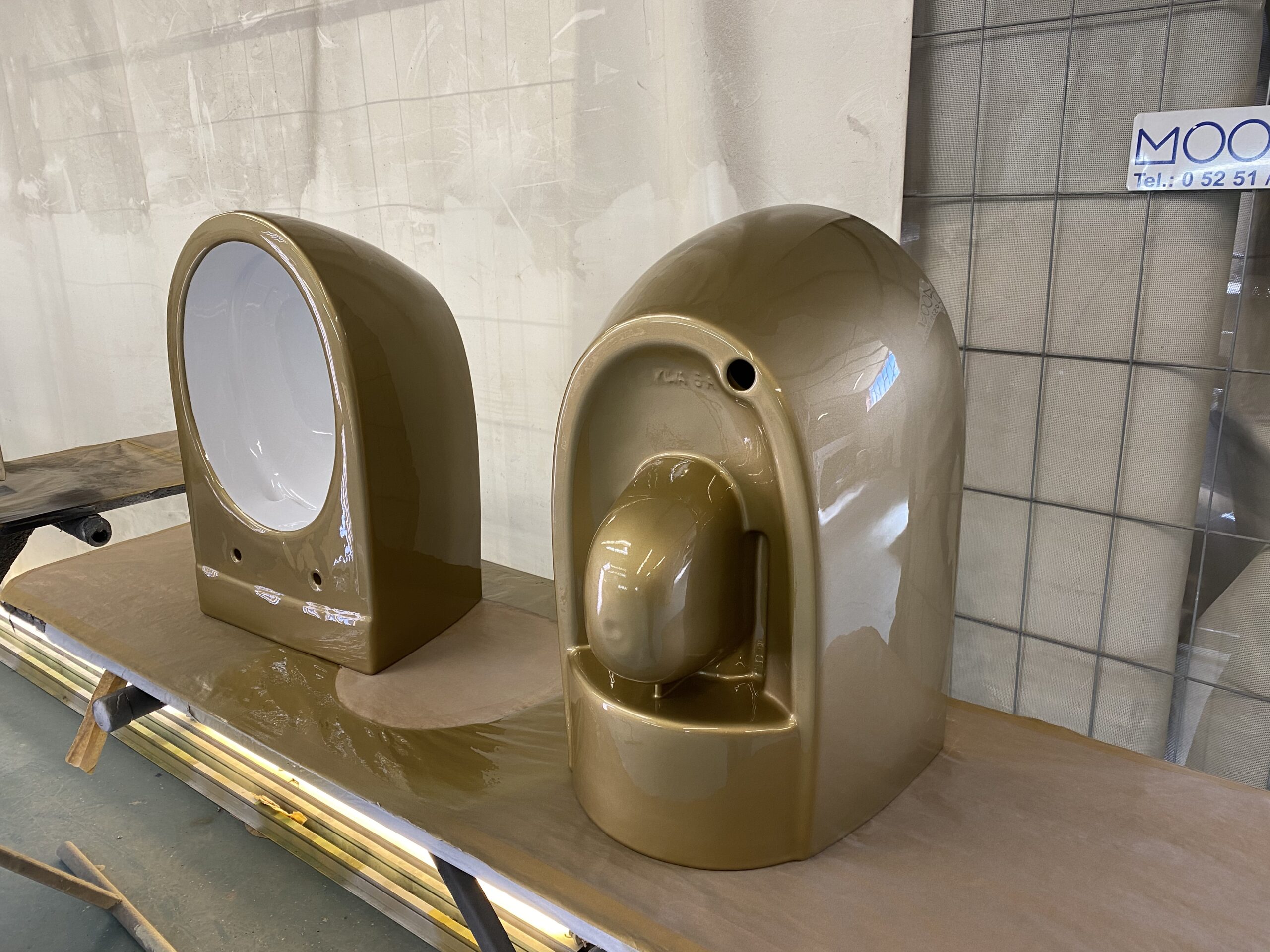 Zwei goldbraun lackierte Sanitärgehäuse auf einem Arbeitstisch in einer Werkstatt
