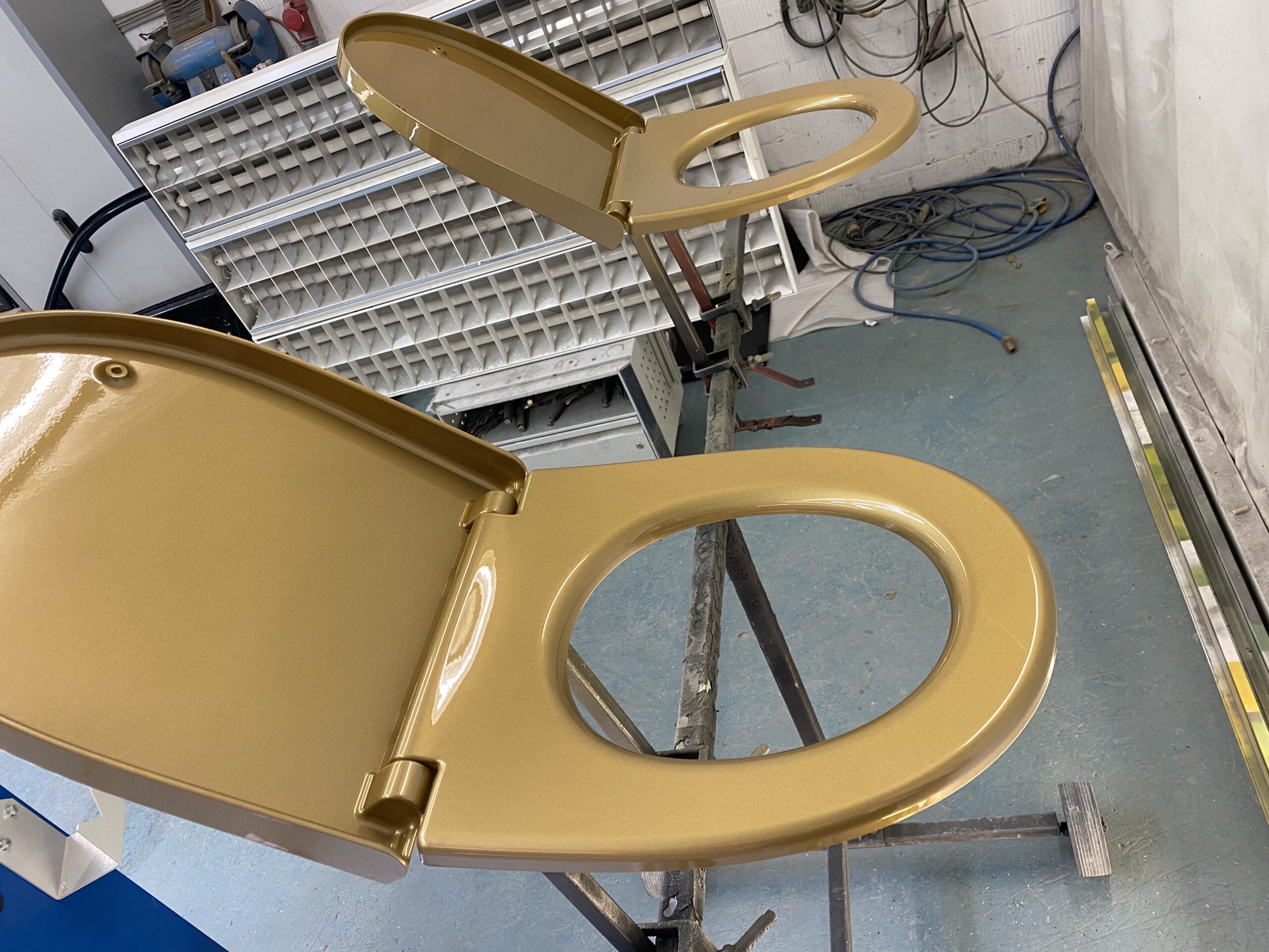Goldene Toilettensitze auf einem Gestell in einer Werkstatt mit Kabeln und Lagerregalen
