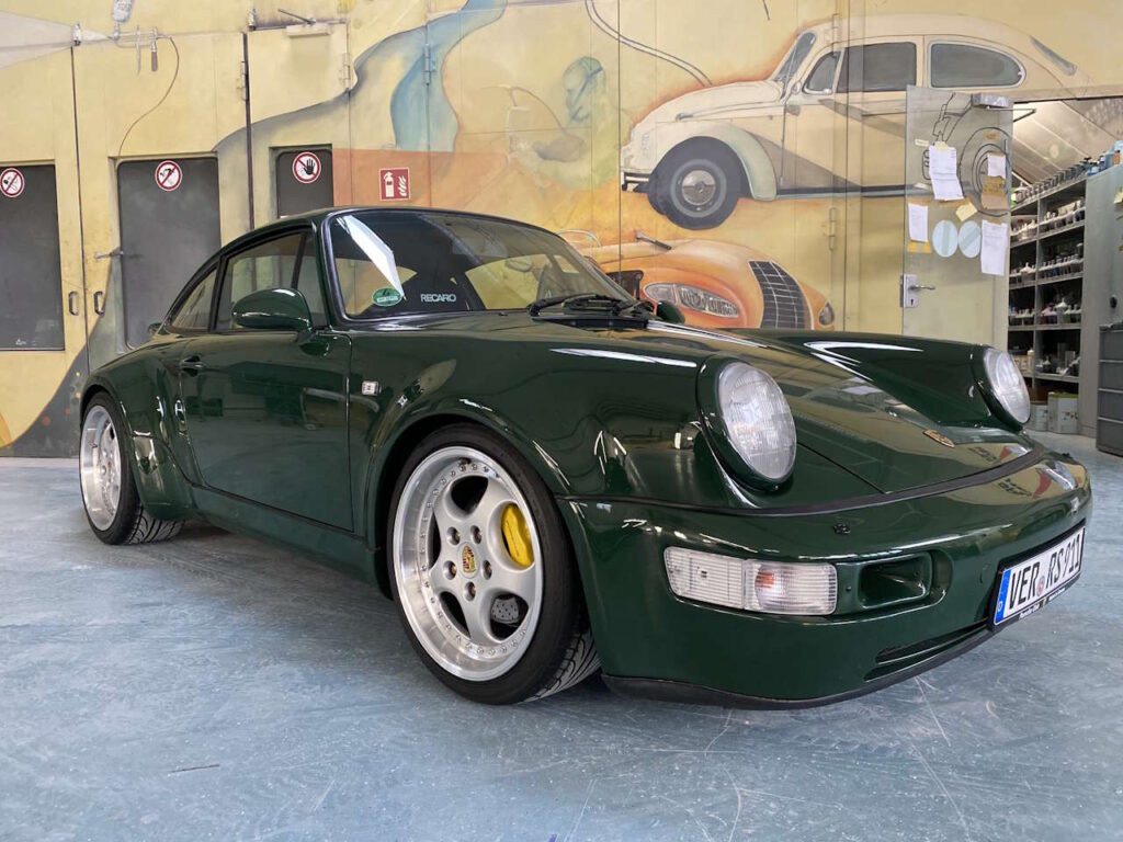 Dunkelgrüner klassischer Porsche 911 in einer Werkstatt, mit breiten Felgen und niedrigem Fahrwerk